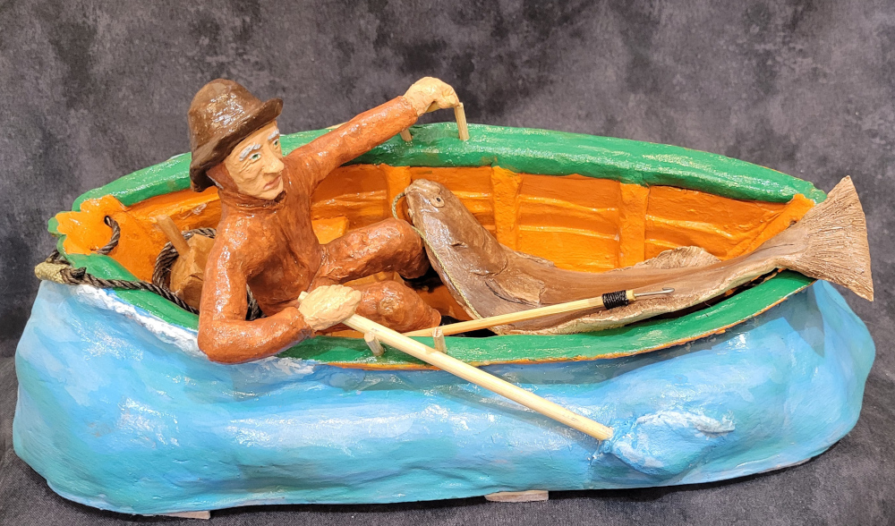 A carvng of a Cape Island fisherman on a wharf with small Cape Island boats.